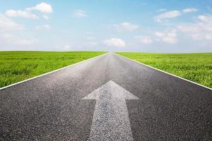 Arrow sign pointing forward on long empty straight road, highway photo