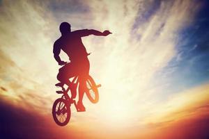 Man jumping on bmx bike performing a trick against sunset sky photo