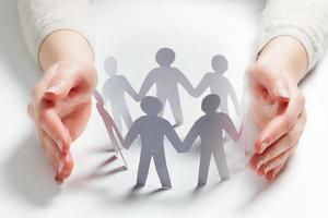 Paper people surrounded by hands in gesture of protection. Concept of insurance