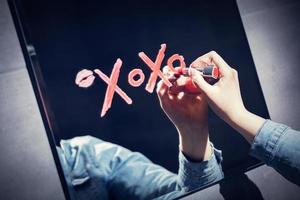 mujer escribiendo xoxo en un espejo con lápiz labial rojo. foto
