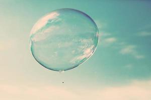 One clean soap bubble flying in the air, blue sky. Vintage photo