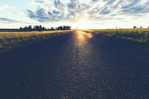 carretera asfaltada, un campo de hierba y puesta de sol. foto