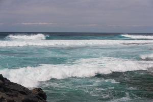 Turbulent ocean waves with white foam beat coastal stones photo