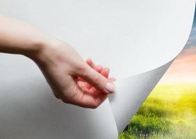 Hand pulling a paper corner to uncover, reveal green landscape photo