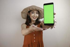 Excited and smiling young Asian woman showing green screen at smartphone in her hand photo