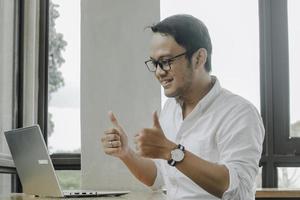 Young Asian man doing video conference on laptop computer while sitting at the cafe, having meeting photo