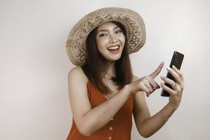 Excited and smiling young Asian woman pointing finger at smartphone in her hand photo