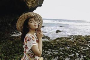 una joven asiática con sombrero de playa se relaja en la playa del cielo azul en gunungkidul, indonesia foto