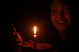 mujer asiática sonriendo a su celular con velas en la noche oscura foto