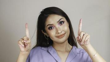 Portrait of beautiful young Asian woman smiling and pointing fingers upward at copy space isolated over white background photo