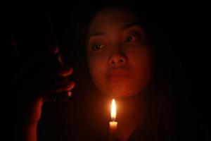 mujer asiática mirando su teléfono con velas en la noche oscura foto