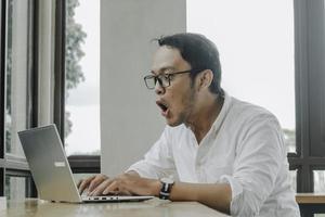 Surprised businessman looking at laptop screen, male office worker suffering business problems while working online on computer in office photo