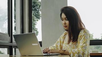 Young Asian woman working on laptop computer while sitting at the cafe, looking through documents photo