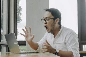 Surprised businessman looking at laptop screen, male office worker suffering business problems while working online on computer in office photo