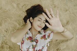 A young beautiful Asian woman dazzled by the light while lying on the beach sand photo