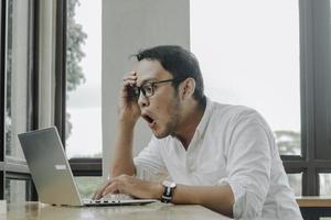 Surprised businessman looking at laptop screen, male office worker suffering business problems while working online on computer in office photo