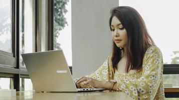 Young Asian woman working on laptop computer while sitting at the cafe, looking through documents photo