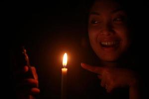 Asian woman smiling to her cellphone with candle in the dark night photo