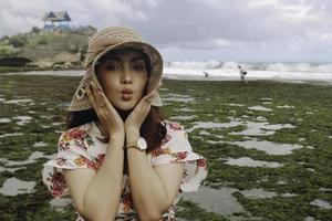 una joven asiática que lleva un sombrero de playa se relaja en la playa del cielo azul en gunungkidul, indonesia foto