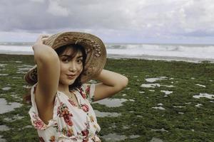 una joven asiática con sombrero de playa se relaja en la playa del cielo azul en gunungkidul, indonesia foto