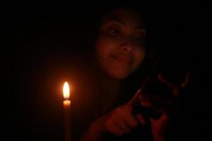 mujer asiática sonriendo a su celular con velas en la noche oscura foto