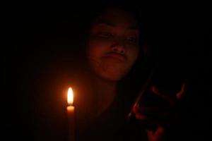 Asian woman looking at her phone with candle in the dark night photo