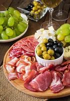 Plato de catering antipasto con tocino, cecina, salami, queso y uvas sobre un fondo de madera