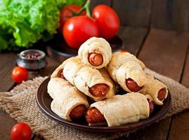 Sausage in the dough sprinkled with sesame seeds on a wooden background in rustic style photo