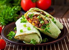 Burritos wraps with minced beef and vegetables on a wooden background photo