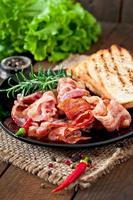 Fried bacon and toast on a black plate on a wooden background photo