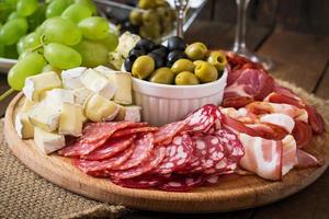 Plato de catering antipasto con tocino, cecina, salami, queso y uvas sobre un fondo de madera foto