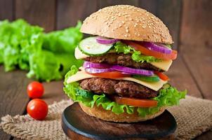 Gran jugosa hamburguesa con verduras y carne sobre un fondo de madera en estilo rústico foto