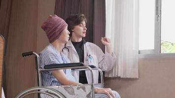 Uniformed young Caucasian female therapy doctor encouraging wheelchair male patient at window to support and motivate recovery, cancer illness after chemo medical treatment in hospital inpatient room. video