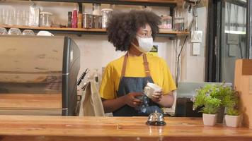 une barista afro-américaine travaille en nettoyant une tasse de café, en regardant à travers la fenêtre du café, en attendant les clients dans un nouveau service de style de vie normal, l'impact commercial des PME de la quarantaine pandémique covid19. video