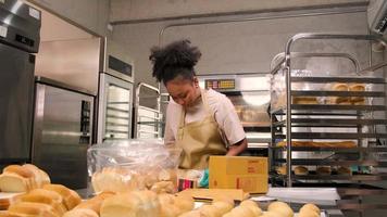 bakkerij opstarten kleine bedrijven levering. een afro-amerikaanse vrouwelijke kok verpakt handgemaakt en vers gebakken brood en gebak in dozen en verzendt online klantaankopen in de culinaire keuken. video