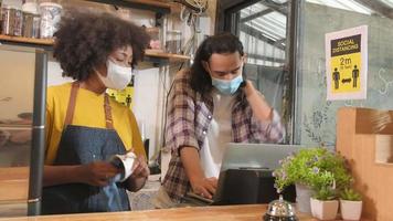 dos jóvenes cafe baristas socios y empresarios en delantales trabajan con máscaras faciales en una cafetería, trabajos de puesta en marcha de servicios en un nuevo estilo de vida normal, impacto empresarial de la cuarentena pandémica covid19. video