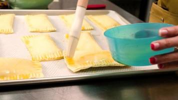 Close-up shot of a chef's hands with apron coats creams caramel from egg yolks into pastry dough with a paintbrush before baking a pie and bakery foods at a kitchen of culinary cooking course class. video