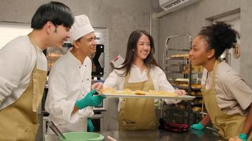 jovem estudante de culinária asiática mostra bandeja de tortas assadas no forno, cheiro bom para grupo de chefs, cozinha de pastelaria feliz na aula de culinária, ocupação de alimentos na cozinha de aço inoxidável.