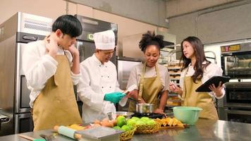 corso di cucina per hobby, lo chef maschio senior in uniforme da cuoco insegna ai giovani studenti delle lezioni di cucina a preparare, mescolare e mescolare gli ingredienti per i pasticcini, le torte di frutta nella cucina in acciaio inossidabile del ristorante. video