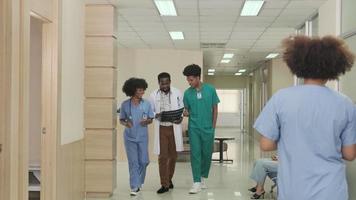 gruppe von praktizierenden team, professioneller afroamerikanischer männlicher arzt mit medizinstudenten gehen und diskutieren diagnose-röntgenfilm in der internationalen ambulanten gesundheitsklinik im thailändischen krankenhaus. video