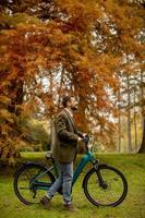 Apuesto joven con bicicleta eléctrica en el parque de otoño foto