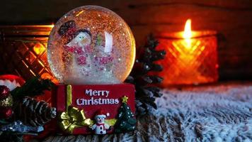 albero di natale, giocattolo di babbo natale e pupazzo di neve nel globo di neve con candele accese per il nuovo anno o le vacanze di natale internazionali su sfondo di legno