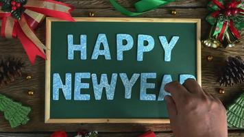 a mão do papai noel colocou letras de madeira para a palavra feliz ano novo no quadro-negro.