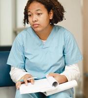 Tired female medical student sitting with study book, portrait. Black intern doctor in uniform exhausted from overworked in a hospital during academic qualification. Professional healthcare occupation photo