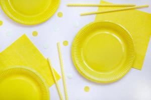 Yellow paper disposable plates, napkins and straws for drinks on white background. Table setting for picnic. Bright eco-court. Birthday, party and holiday concept. Top view, flat lay. photo