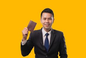 Asian businessman holding passport showing and smiling isolated on yellow background. Business concept. photo