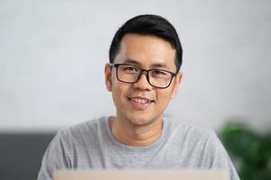 freelance man in eyewear smiling and working with laptop remotely, sitting at wooden table. Pleasant happy man communicating in social network, searching information online. photo