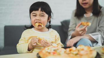 Asian mothers and children do activities at home. Mother is going to feed pizza for her kids. Children are eating and tasting italian homemade pizza. photo