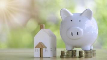 White piggy bank on gold coins stack 4 rows with home placed on wooden table to save money invest for future.Concept for loan, property ladder, financial,real estate investment, tax and bonus. photo