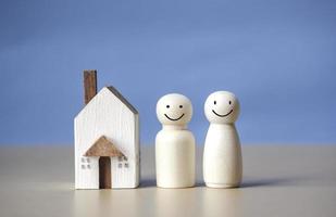 Two wooden figures of people with happiness and a house on blue background. Affordable housing and mortgages for buying concept young family and couples. family nest and copy space. photo